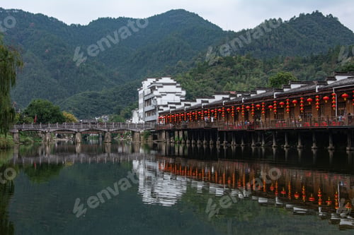 Preview: Chinese buildings with red lanterns reflected in a calm river with mountain in the background