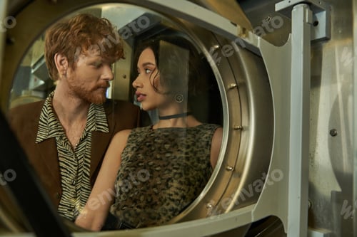 Preview: stylish interracial romantic couple posing near washing machine in public laundry