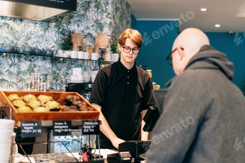 Preview: Young waiter serving customer at cash point in cafe. Man working with POS terminal. Cashier, barista