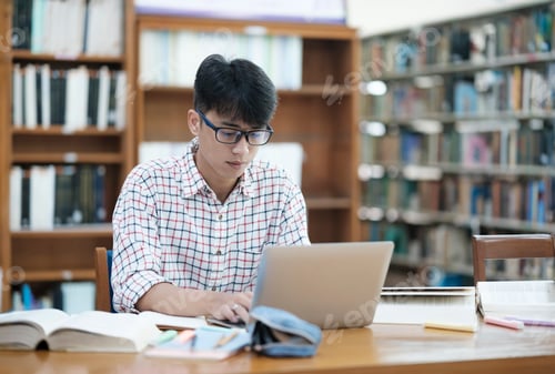 Preview: Young Asian male sitting inside a library alone doing research.