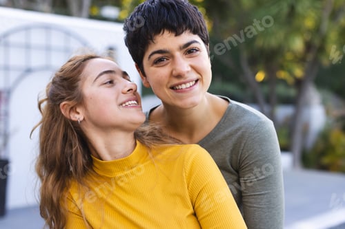 Preview: Portrait of happy biracial lesbian couple standing on garden terrace embracing and smiling
