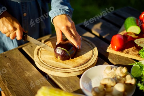 Preview: Unrecognizable woman cutting fresh eggplant vegetables on wooden board