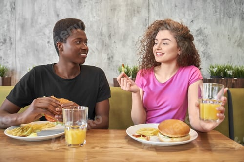 Preview: Young woman and man eating hamburgers, french fries in cafe