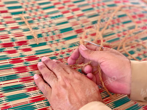 Preview: Diverse unrecognizable man weaves a colorful mat carefully with his skillful hands