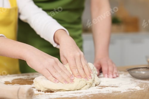 Preview: Making bread. Mother and her daughter kneading dough at wooden table in kitchen, closeup
