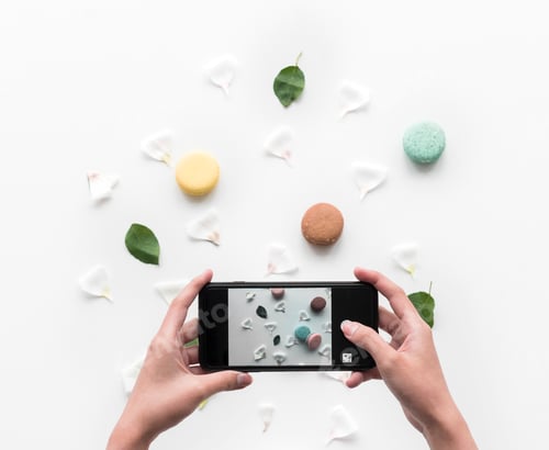 Preview: Hands holding a smart-phone capture a macaroon