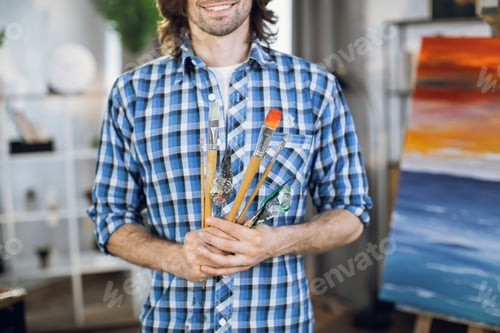 Preview: Male artist holding brushes and spatula in hands