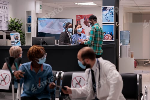 Preview: Young man at hospital reception talking to medical staff