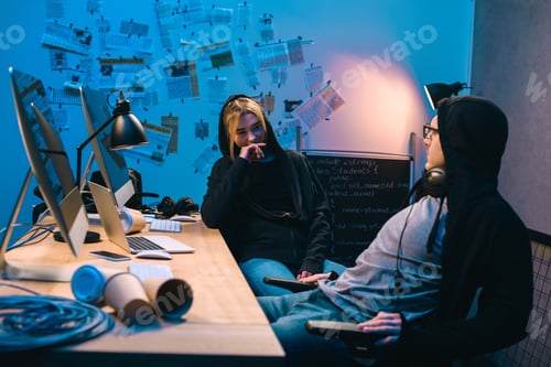 Preview: couple of young hackers chatting at workplace in dark room