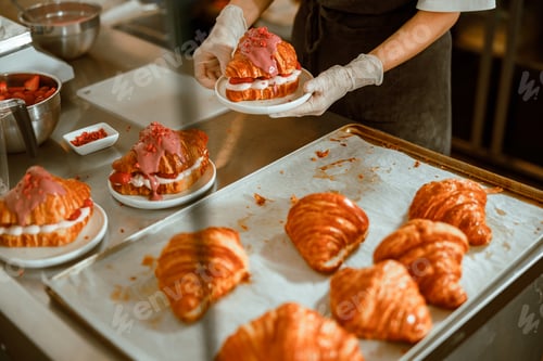 Preview: Confectioner in gloves holds plate with delicious croissant in craft bakery shop