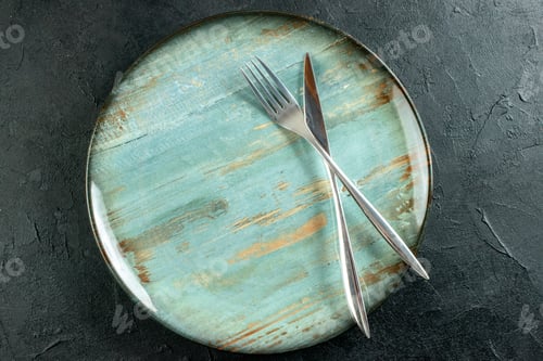 Preview: top view crossed knife and fork on round platter on black background