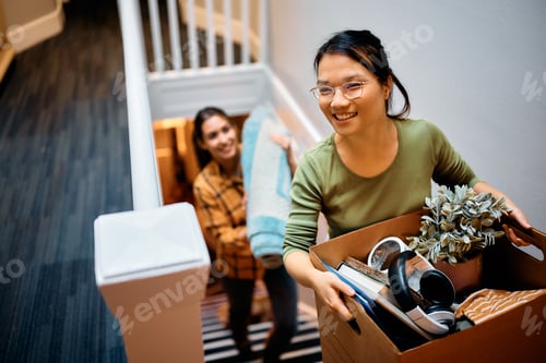 Preview: Happy Asian woman and her friend walking upstairs through hallway while moving in new apartment.