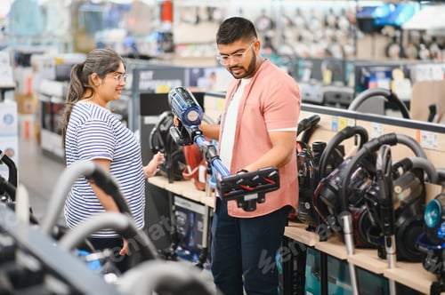 Preview: Young beautiful indian couple buying new vacuum cleaner at tech store
