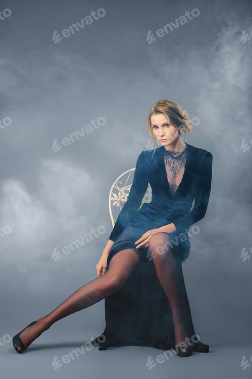 Preview: Full length portrait of beautiful lady in long velvet dress with deep cut sitting on chair.