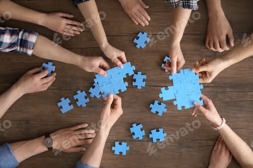 Preview: People with puzzle on wooden background, closeup of hands. Unity concept