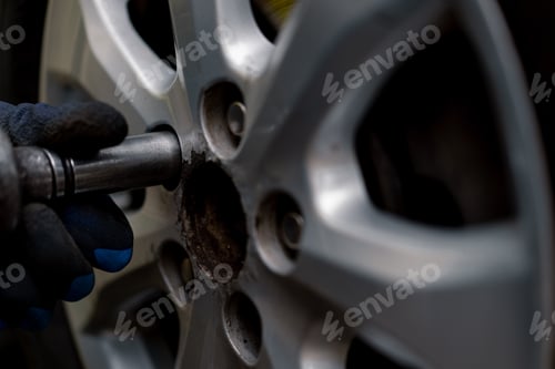 Preview: Auto mechanic in changing a wheel from a black car using a drill in a tire shop on the street