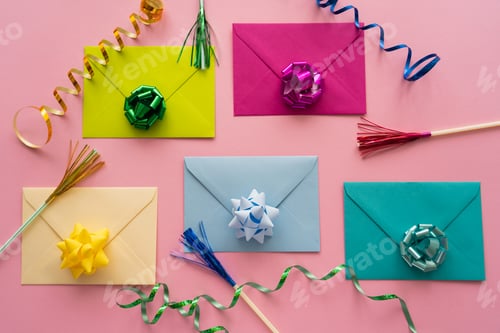 Preview: Top view of colorful gift bows on envelopes near serpentine on pink background