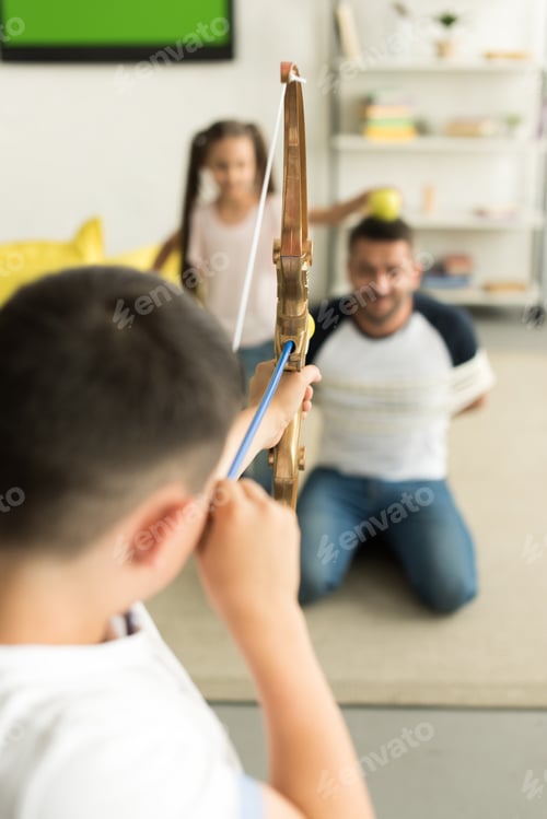 Preview: selective focus of children playing with tied father and pretending shooting with toy bow at home