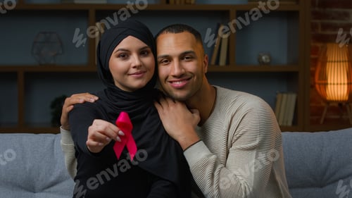 Preview: Multiracial family muslim woman and african american man sit on sofa indoors hold red ribbon prevent