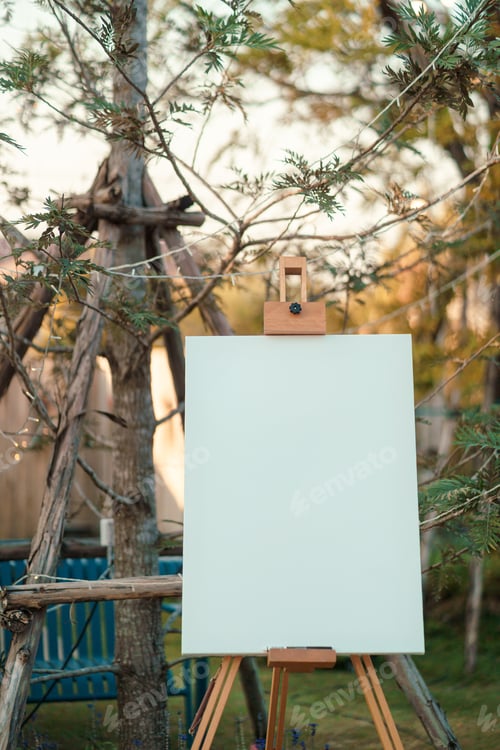 Preview: Blank canvas set on wooden easel placed front of wedding event in rustic style