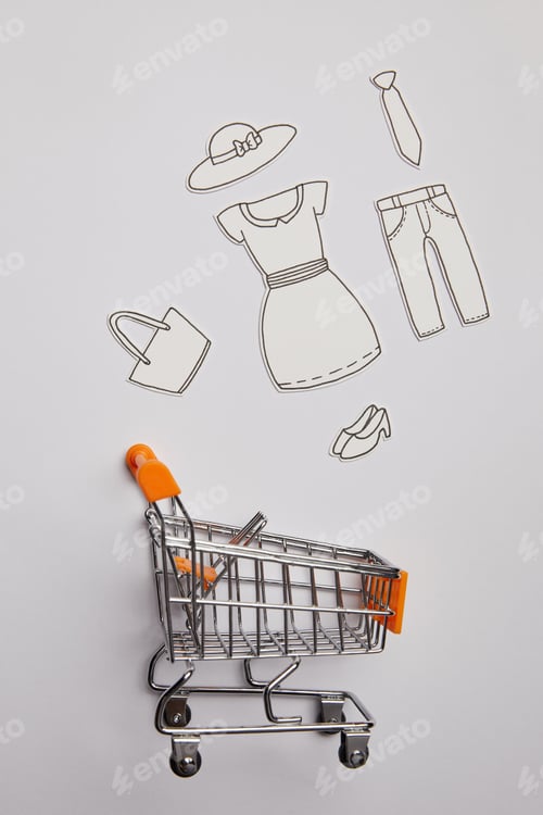 Preview: top view of shopping cart and little clothes made of paper on grey background