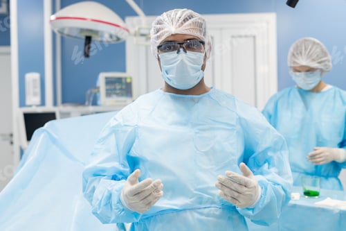 Preview: Contemporary mixed-race male surgeon in protective mask, gloves and eyeglasses