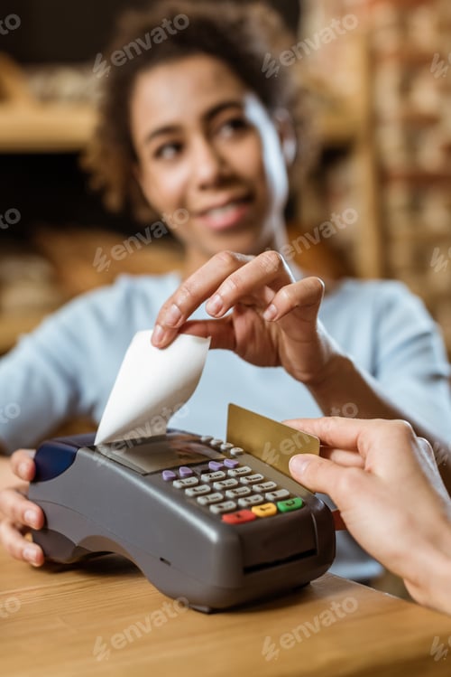 Preview: cropped shot of cashier with pos terminal receiving purchase from client at pastry store