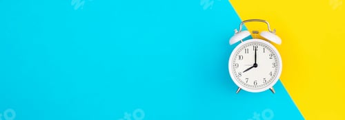 Preview: White alarm clock on a blue and yellow background, flat lay.