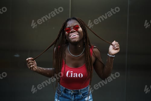 Vista previa: Mujer afroamericana con vitíligo con gafas de sol y riendo mientras sostiene sus trenzas de pelo.