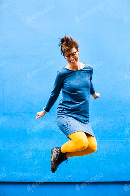 Preview: Full length of cheerful woman jumping against blue wall