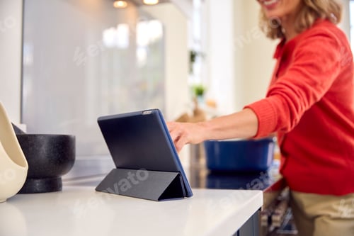 Preview: Close Up Of Mature Woman In Kitchen At Home Cooking Meal Following Recipe On Digital Tablet
