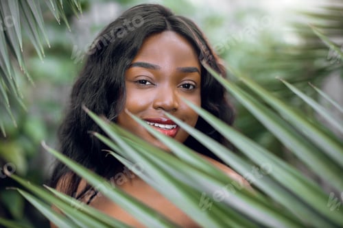 Preview: African woman with healthy skin and natural nude makeup, posing among palm leaves
