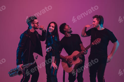 Preview: Group of young multiethnic musicians created band, dancing in neon light on pink background