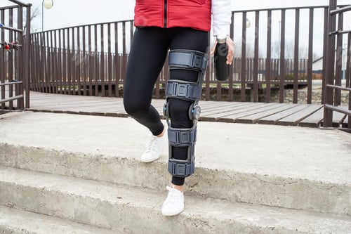 Preview: Woman wearing knee brace or orthosis after leg surgery, walking in the park