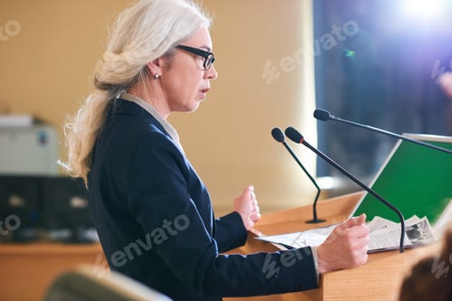 Preview: Mature elegant female delegate in suit speaking in microphone
