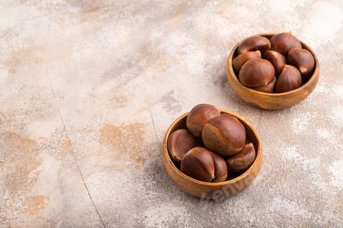 Preview: wooden bowl with raw edible Сhestnuts on brown concrete, side view, copy space, minimalism