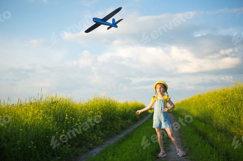 Preview: Girl in a yellow panama hat launches a toy plane into the field. Summer time