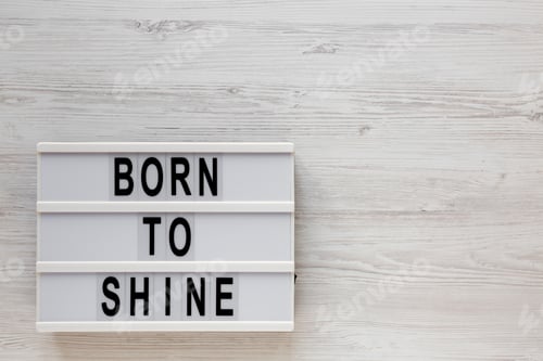 Preview: 'Born to shine' words on a lightbox on a white wooden surface, top view.