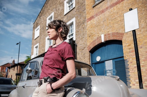 Preview: Non-binary female leaning on antique car enjoying the sun.