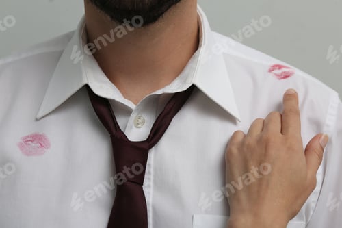 Preview: Woman pointing at lipstick kiss mark on her husband's shirt, closeup