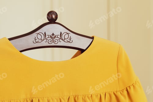 Vista previa: Yellow dress on a wooden hanger. Floor hanger with patterned carving.