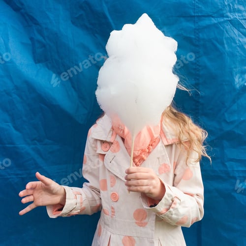 Preview: Girl holding big candy floss in the front of face standing over blue background. Sweet food