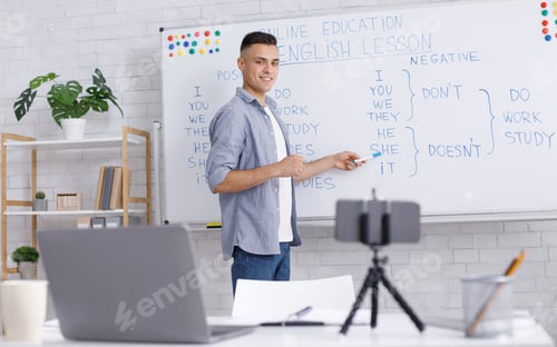 Preview: Online tutor remote. Smiling young man points to whiteboard, looks at webcam