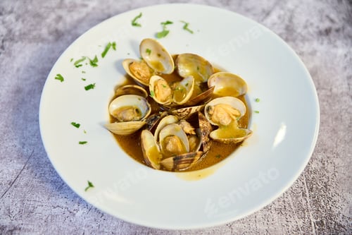 Preview: Plate of steamed clams served in a rich, aromatic brown sauce with a sprinkling of herbs for flavor