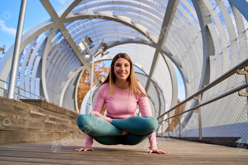 Preview: Young woman practicing yoga asana on modern bridge in the city