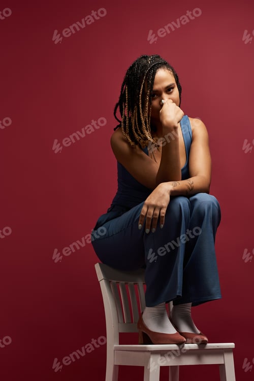 Preview: Stylish young African American woman with braids poses thoughtfully in studio setting