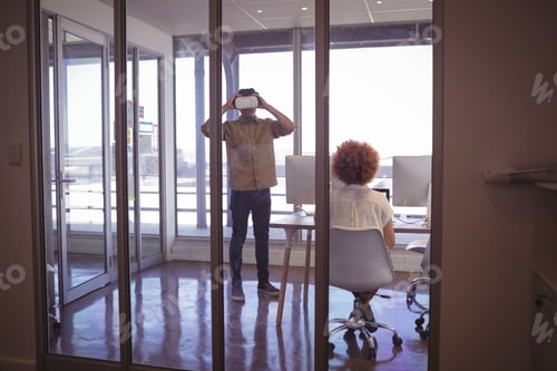 Preview: Female colleague with businessman wearing VR headset in office