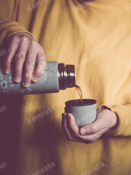 Preview: mid section close up of a woman wearing yellow pouring a cup of coffee from a vintage thermos flask