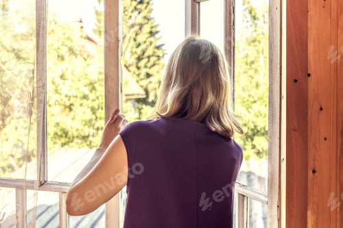 Preview: Young woman opens the window in her country house, looks at the garden