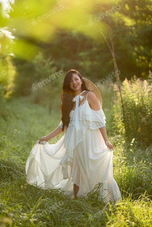 Preview: Pregnant woman posing in a white dress on a background of nature.